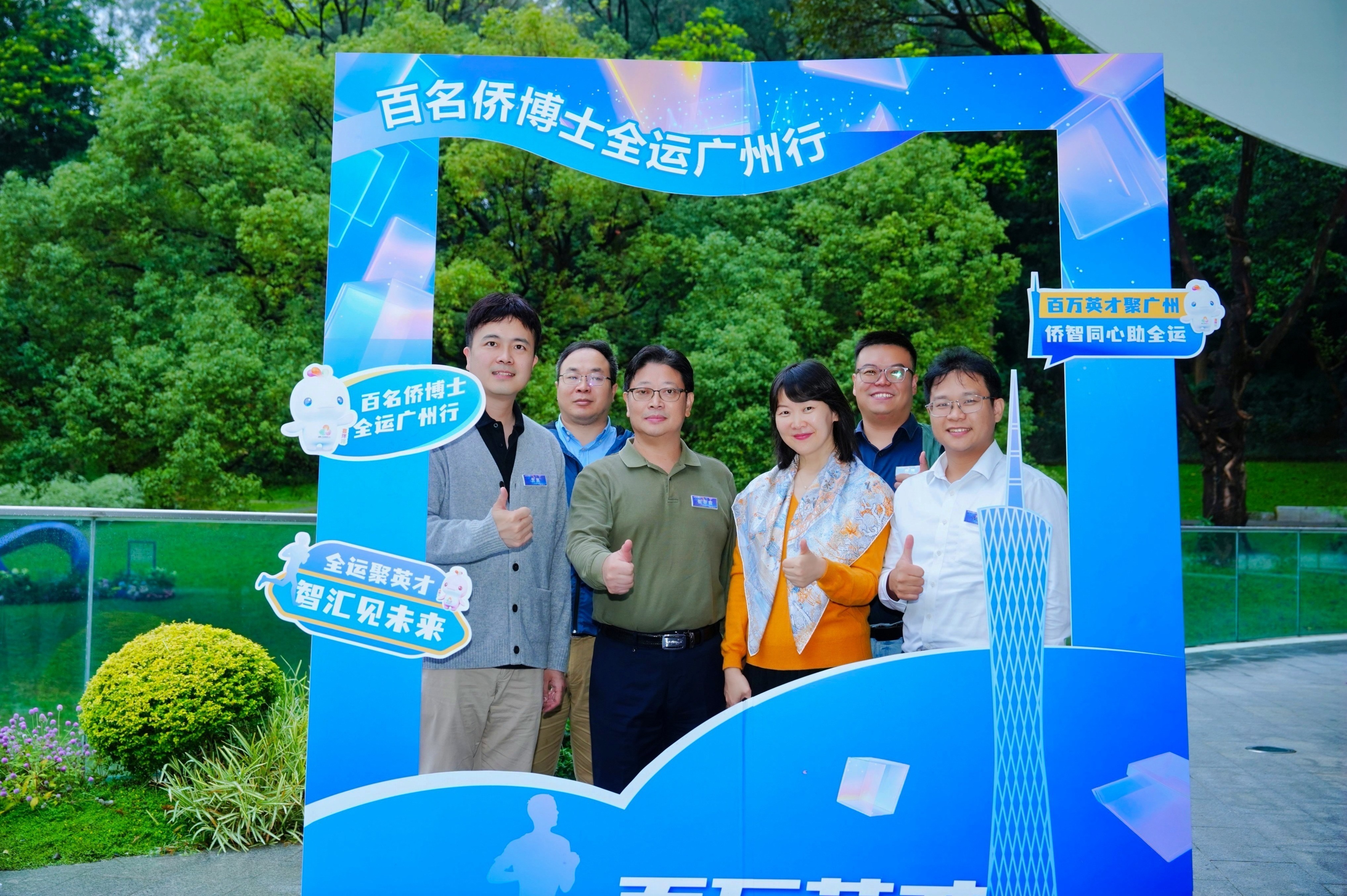 Group of scholars posing at a photo frame reading “百名侨博士全运广州行” during the National Games programme in Guangzhou.